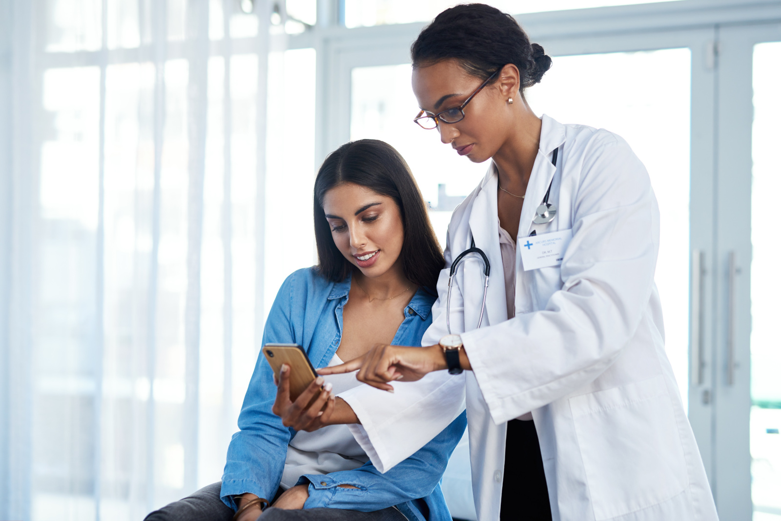 Ill send you some helpful health tips to you. Shot of a young doctor using a smartphone during a consultation with her patient.