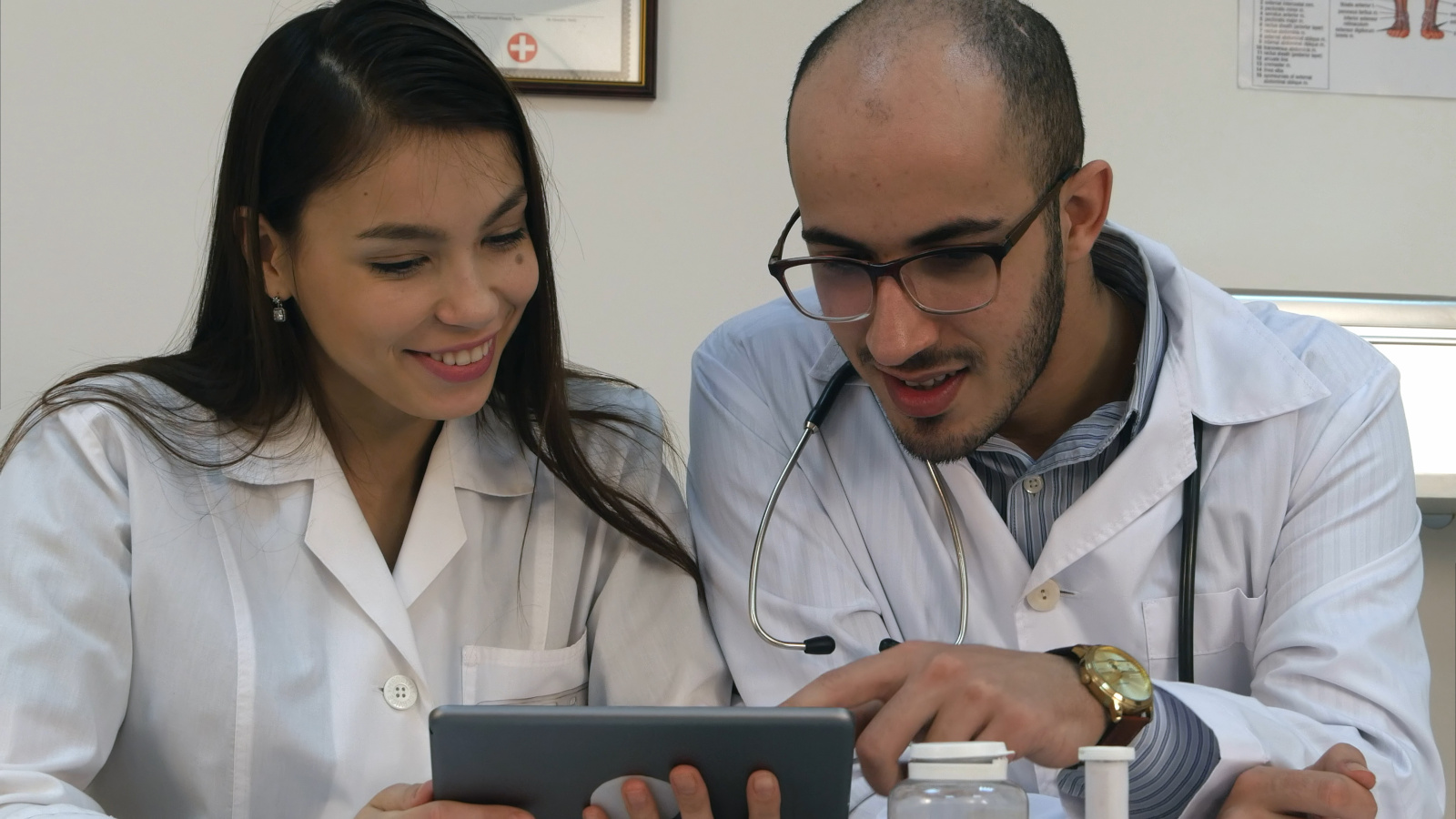 Two doctors looking at something funny on the tablet and laughing Male doctor signing off digital timesheet for female employee. Employee is using the WorkTracker branded timesheet app