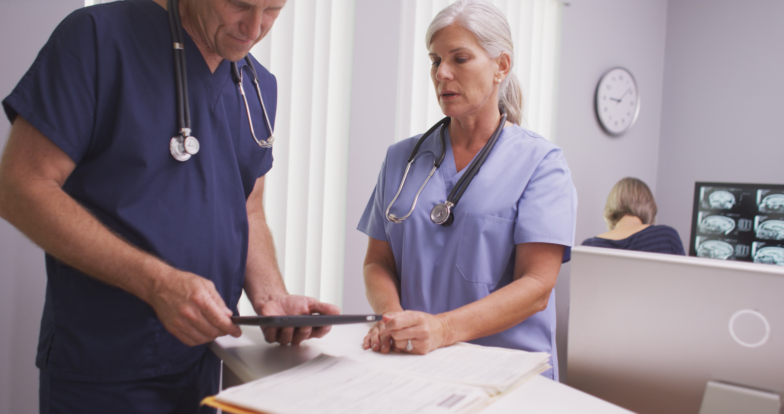 Mature female medical practitioner talking to male colleague at clinic desk