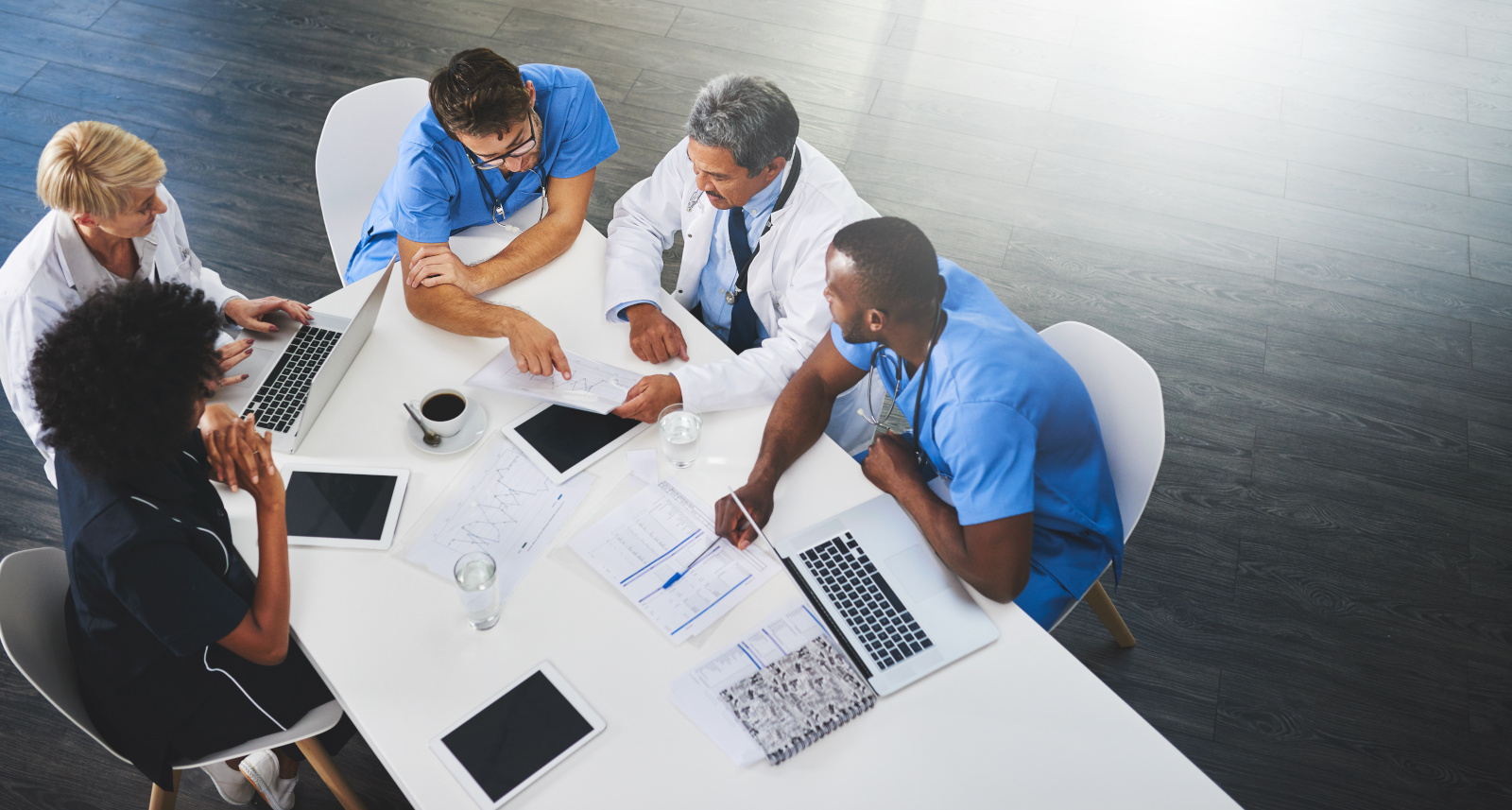 Team of medical workers sitting and meeting with laptops around table. Doctors and staff discussing papers and test results. Healthcare experts handling daily tasks and duties Recruitment agencies client organisation healthcare managers assessing work shift requirements. Working with YouRecruit