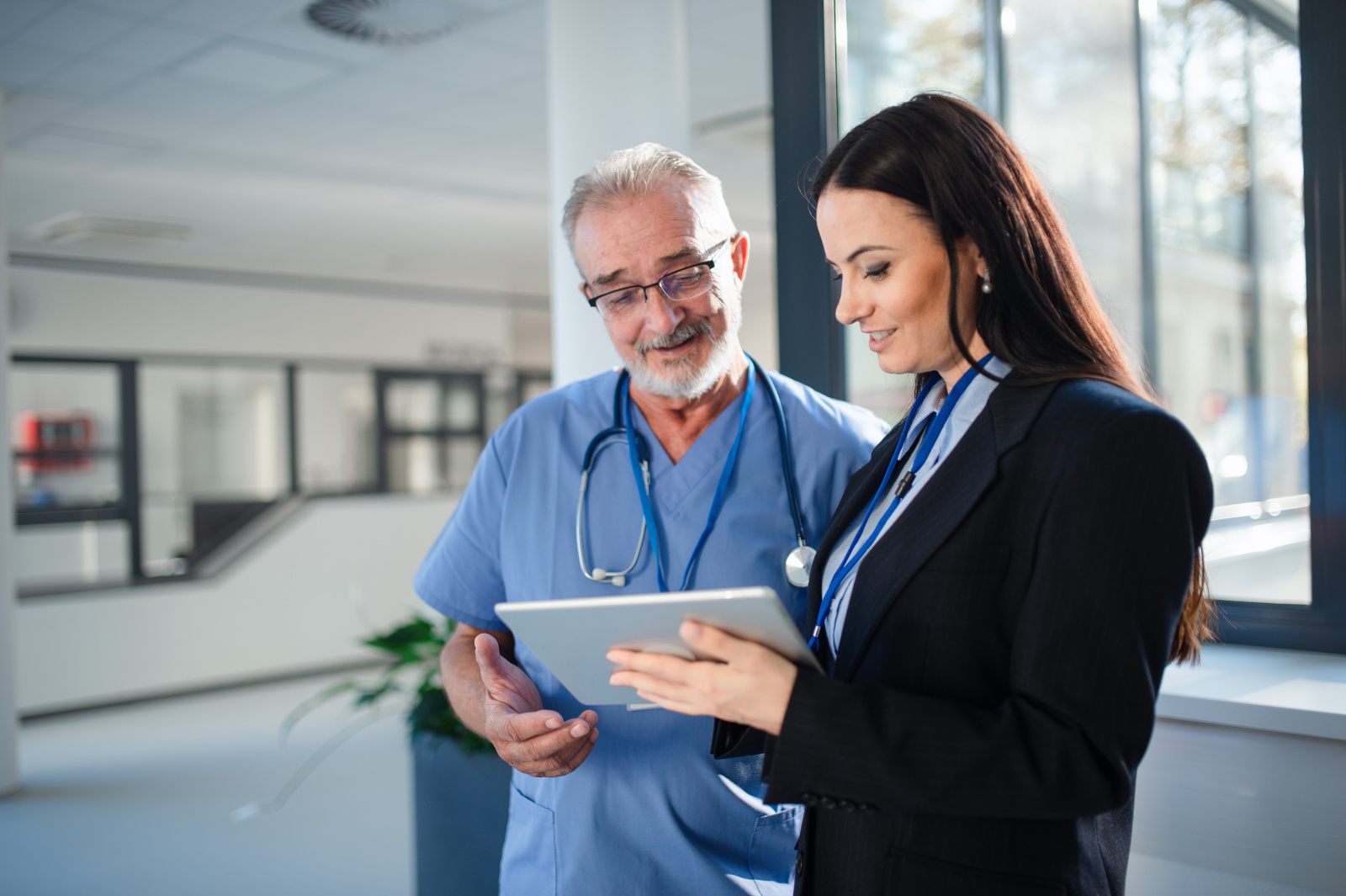 Young pharmaceutic seller explaining something to doctor in hospital. Healthcare manager signing off WorkTracker mobile timesheet for employee