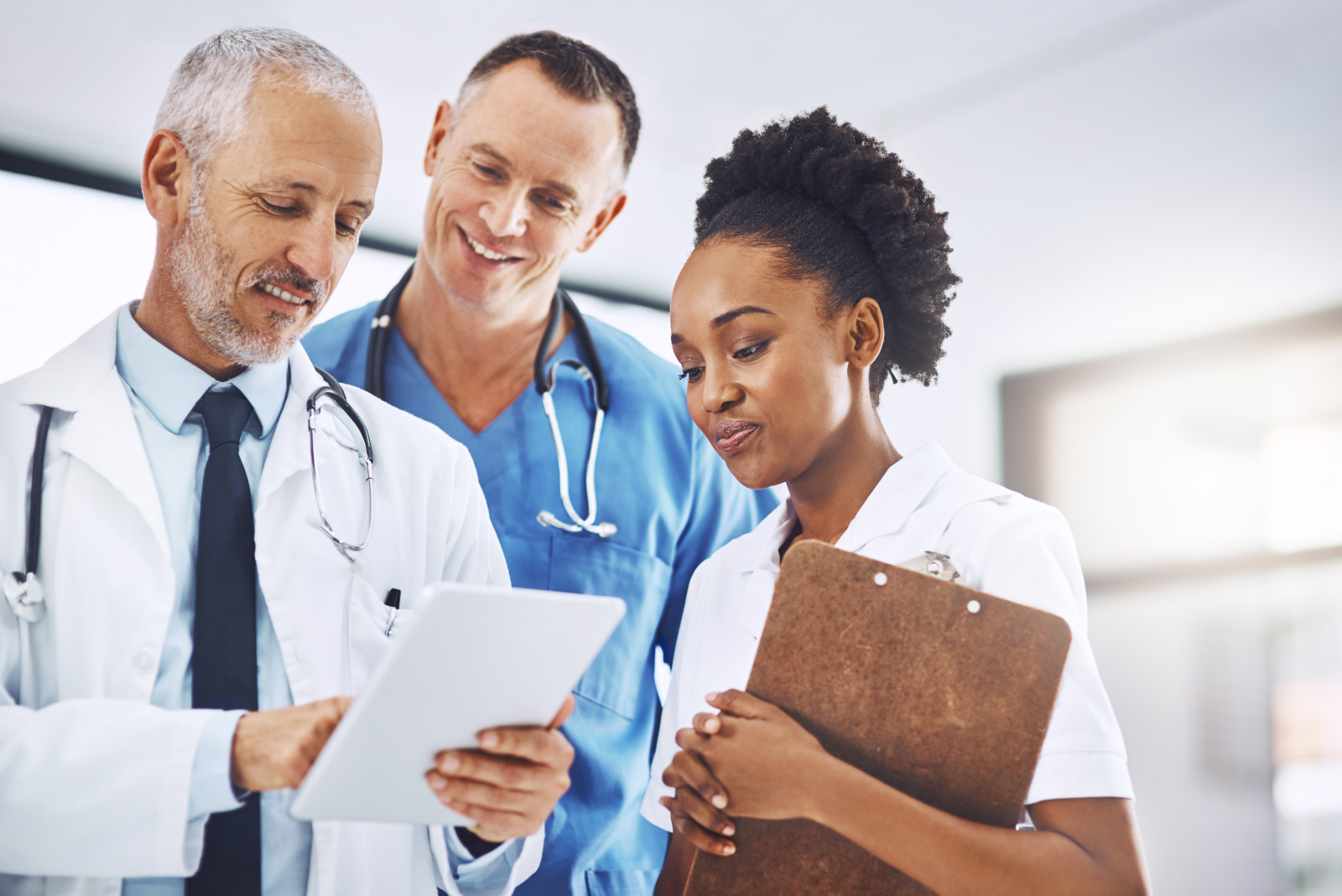 Senior doctor, tablet and coaching team in healthcare for research, teamwork or meeting at hospital. Happy elderly medical professional training staff on technology in group collaboration at a clinic Healthcare shift manager signing off nurse timesheets on a smart device: the WorkTracker mobile timesheet app