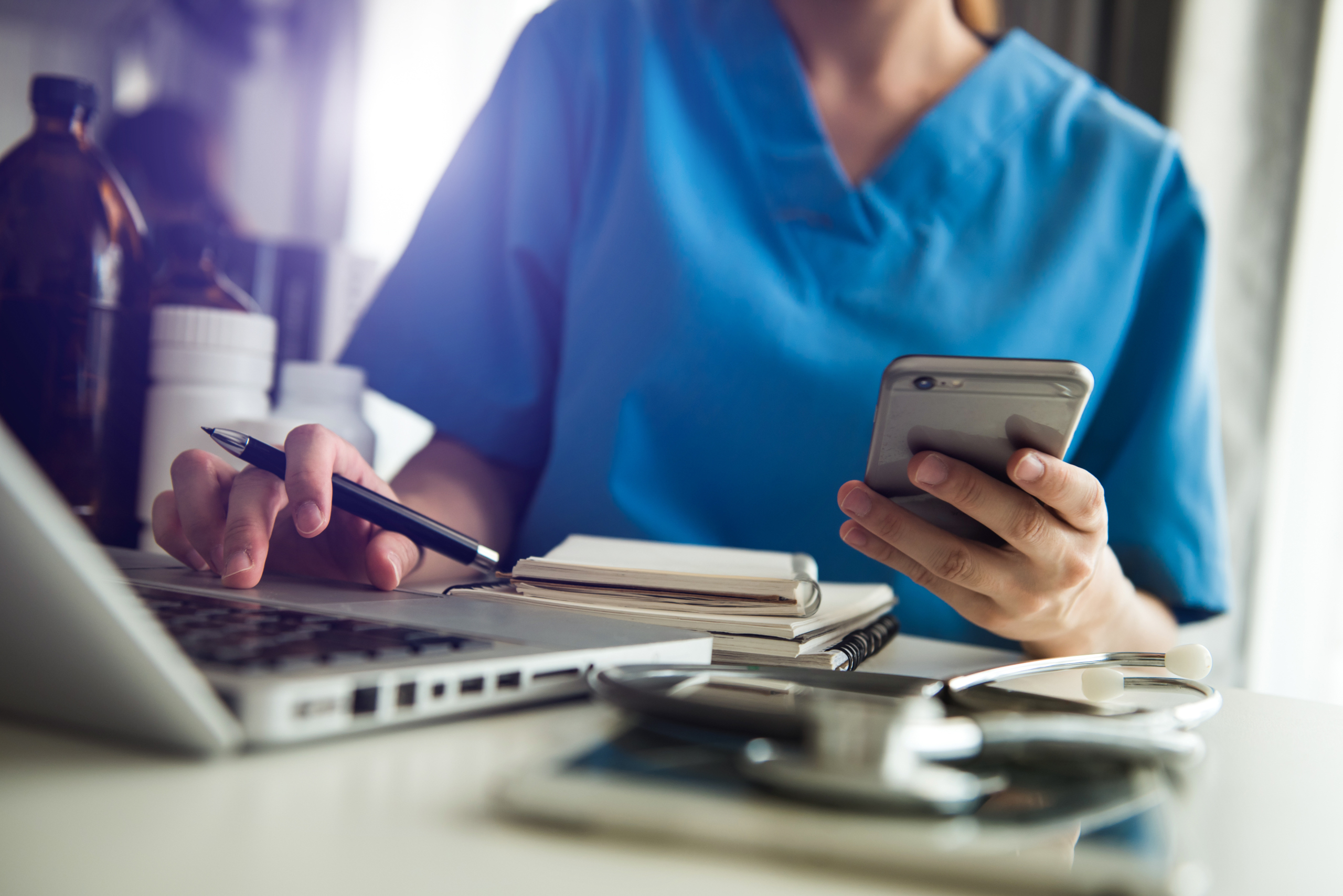 Female healthcare shift manager at desk with laptop and smartphone: YouRecruit compliance administration and staff rota app