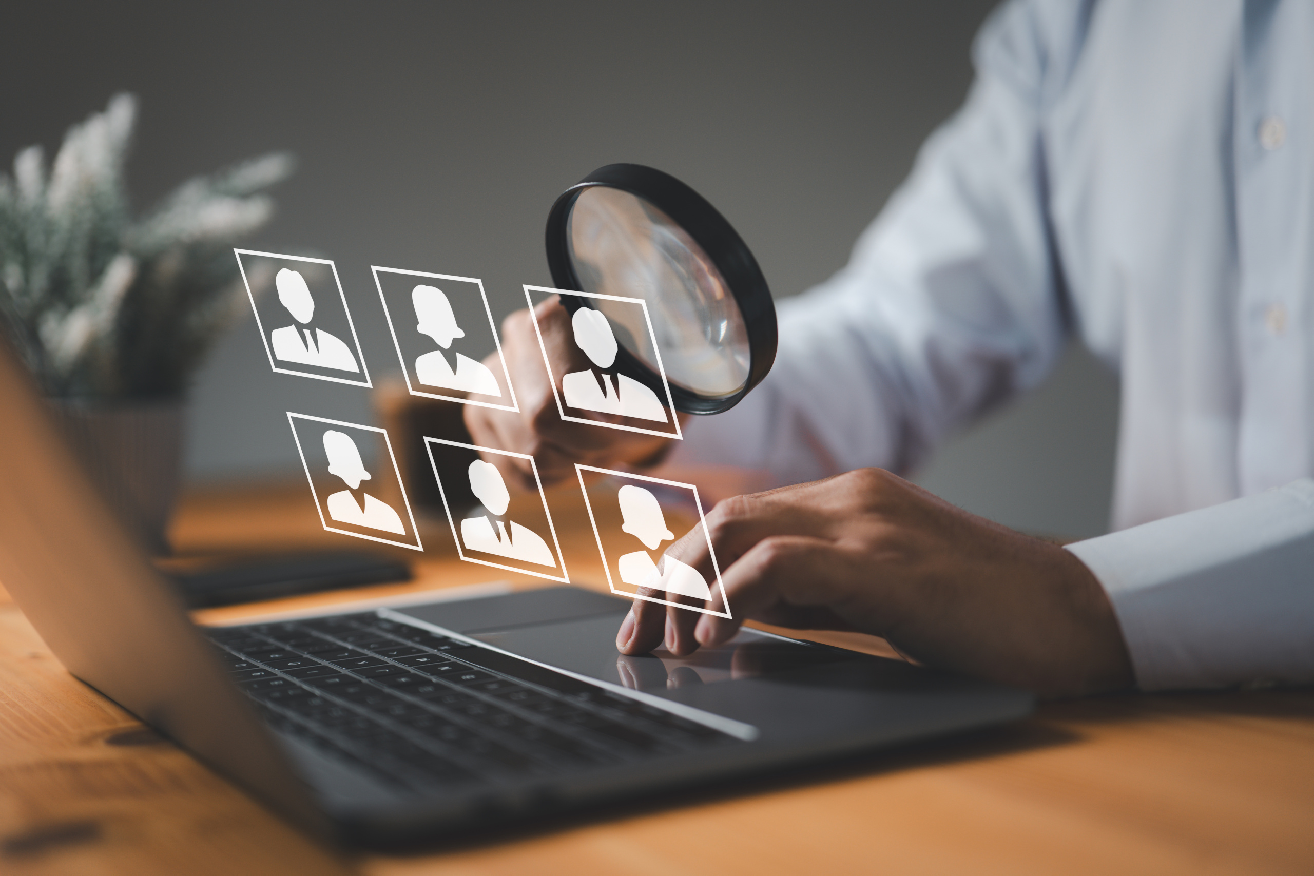 Recruitment agency consultant at desk with laptop and magnifying glass on people icons signifying compliance monitoring