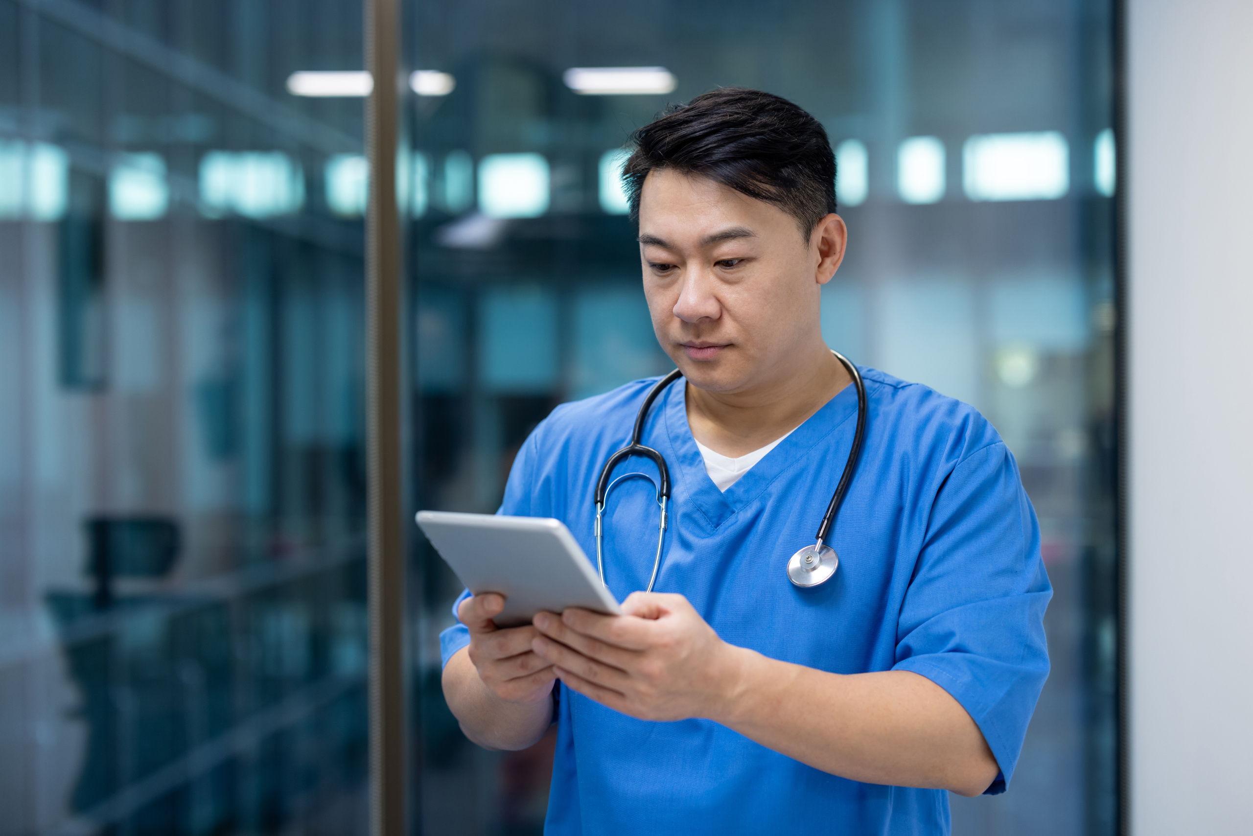 Temporary staff doctor at hospital location wearing scrubs and holding smart device: The WorkTracker healthcare staffing app