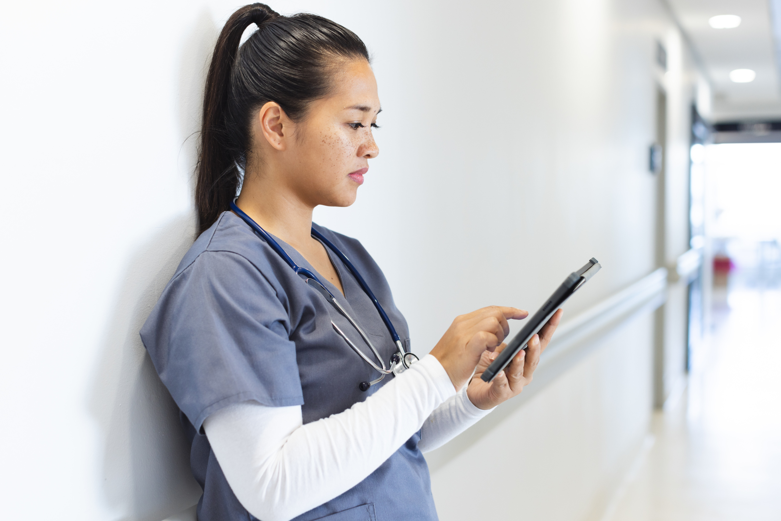 Temporary nurse in hospital corridor looking at smartphone and using the YouRecruit workforce management system: WorkTracker