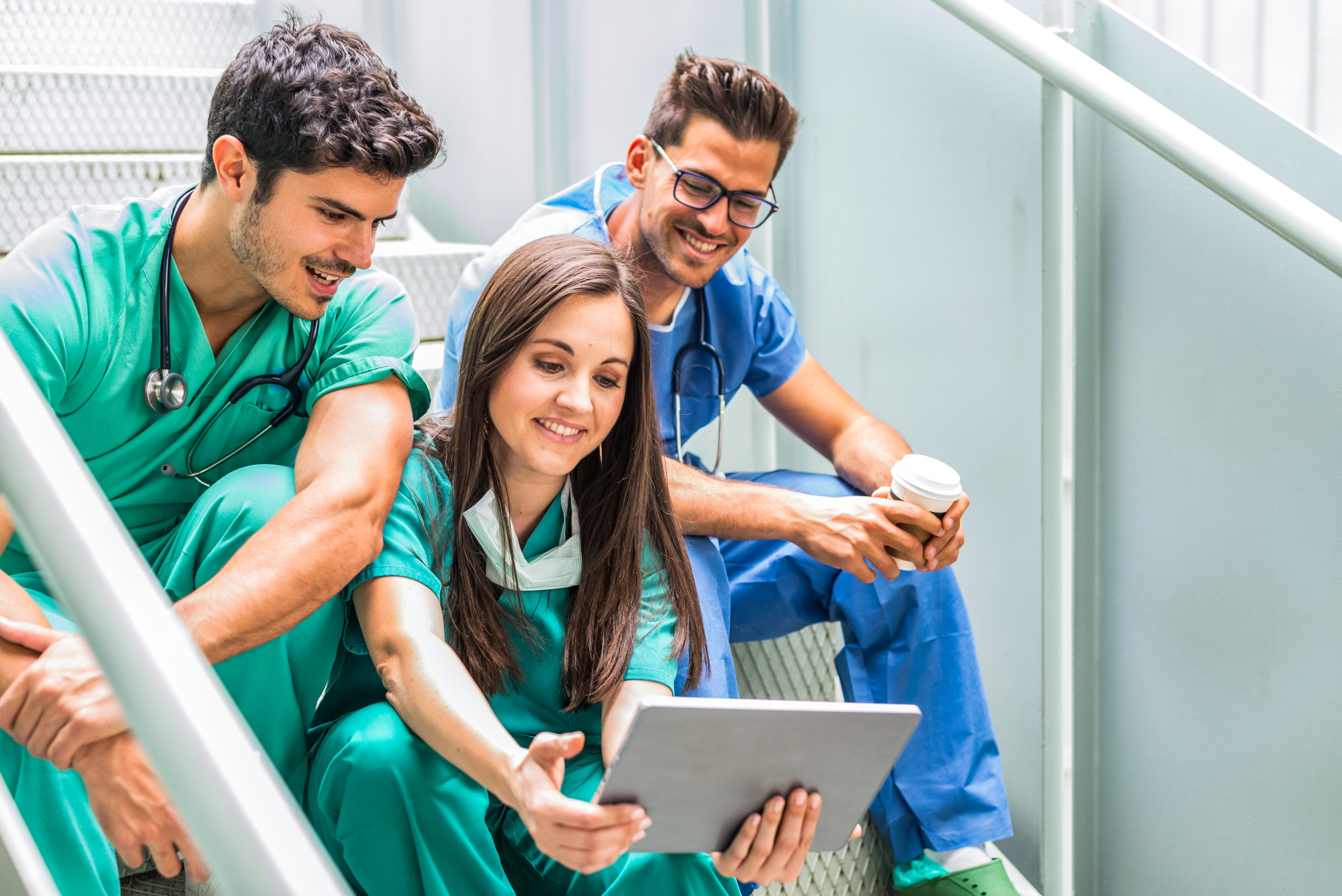 Two male, one female temporary healthcare staff relaxing in stairwell with tablet using the WorkTracker mobile timesheet app