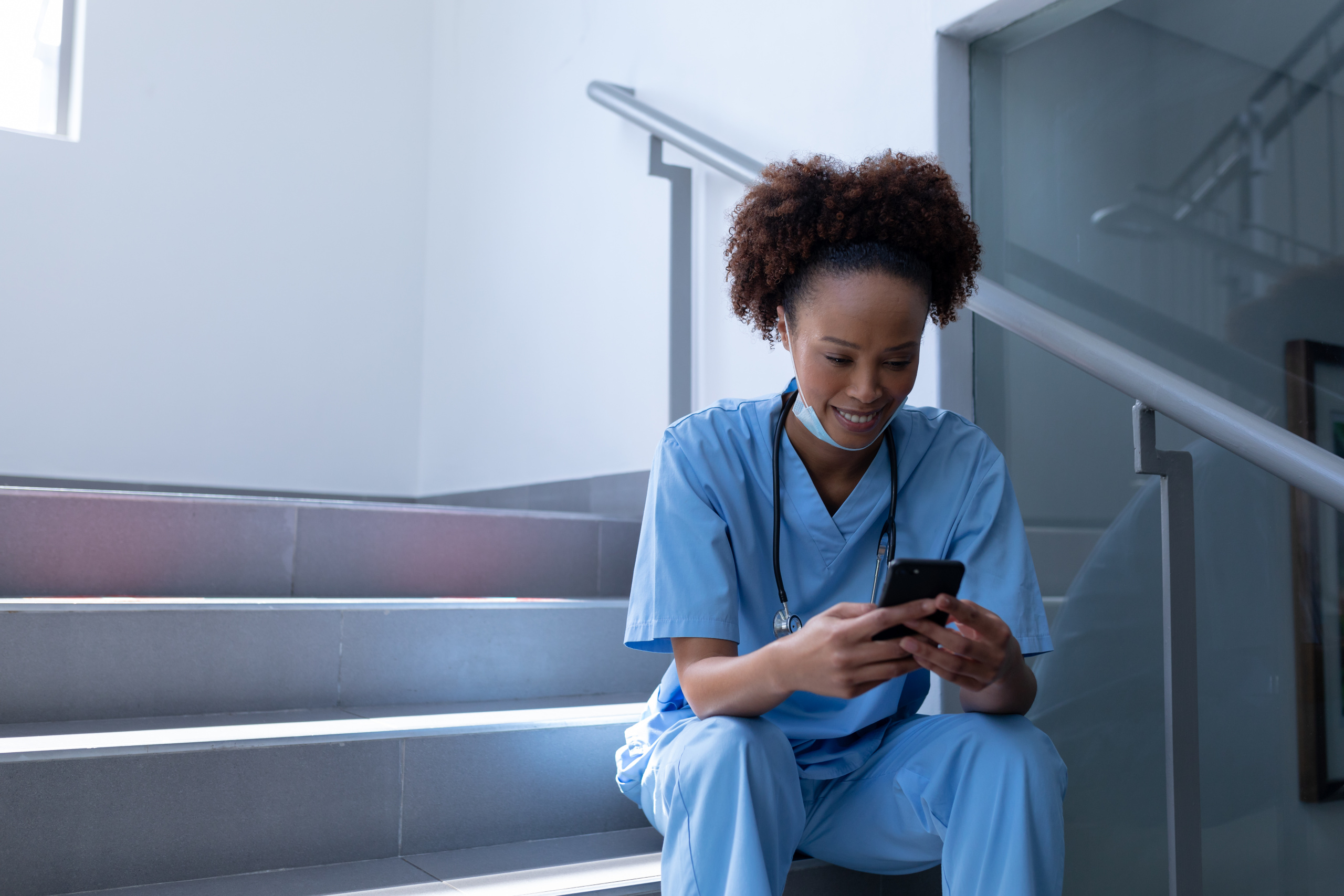 Nurse sitting in a stairwell looking at smartphone and checking employee notifications through the WorkTracker job hours app