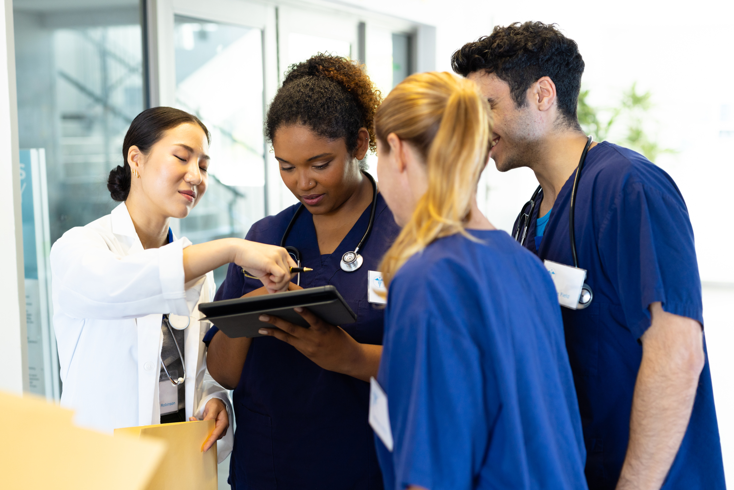 Doctor sharing a tablet with three temporary healthcare employees in hospital corridor: The WorkTracker mobile timesheet app