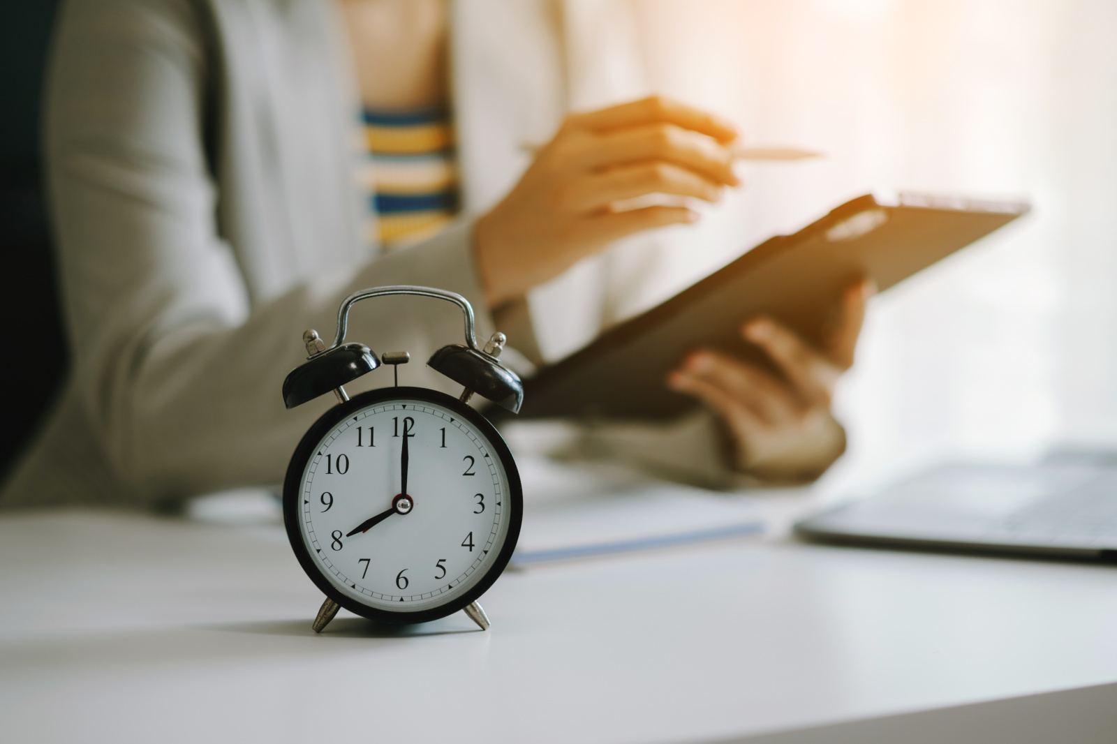 Alarm clock on a desk. Recruitment agency employee with tablet in the background: YouRecruit Time Recording Software