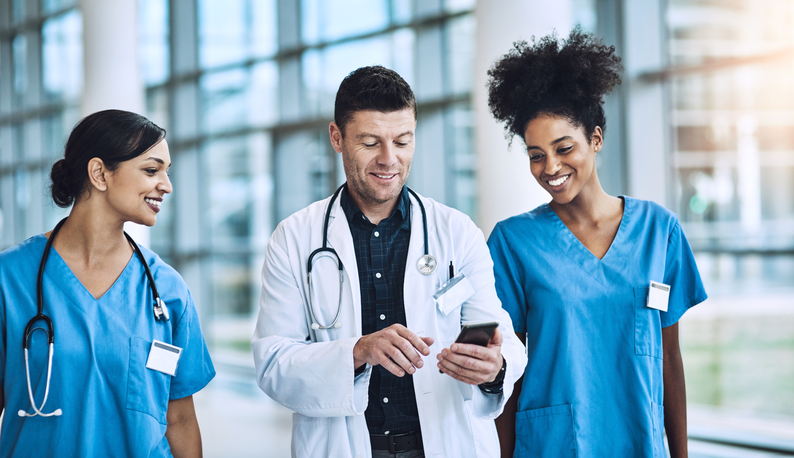 Two female nurses obtaining digital sign-off after completing a shift from male shift manager holding smart phone: YouRecruit