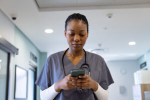 Female nurse in hospital corridor with smart device: The YouRecruit shift scheduling software and workforce management system