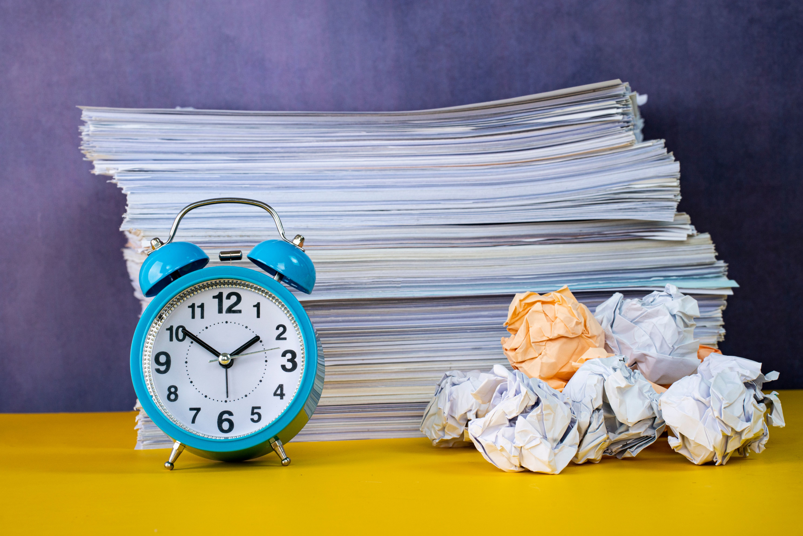 An alarm with crumpled paper in front of a stack of paper timesheets: YouRecruit and WorkTracker Digital timesheets