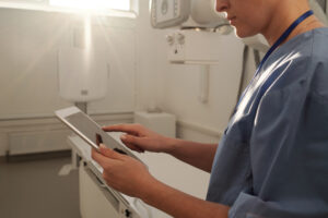 Healthcare professional within an operating theatre holding smart device: The YouRecruit staff communication platform