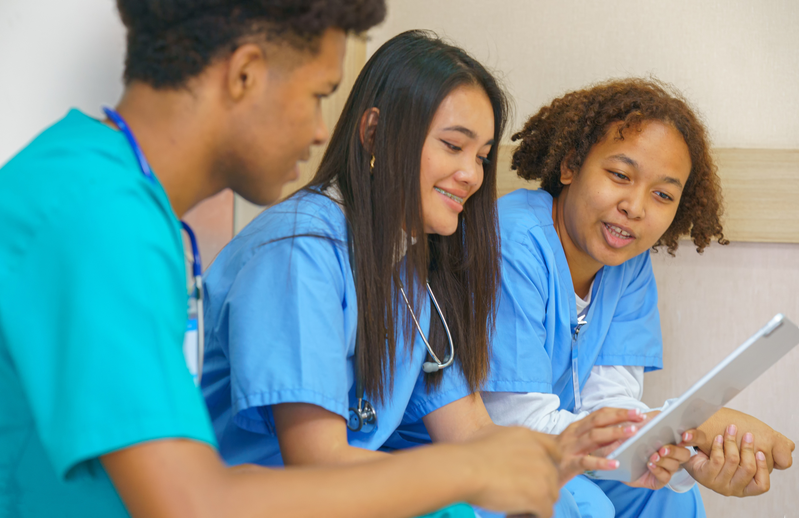 Three young nurses grouped around a tablet using WorkTracker digital timesheets: Recruitment agency timesheet software