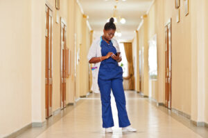 Female nurse in corridor checking the WorkTracker mobile timesheet app on smart phone: The YouRecruit time recording software