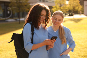 Two happy nurses outdoors in hospital grounds sharing on smart phone. Using the YouRecruit and WorkTracker rota app