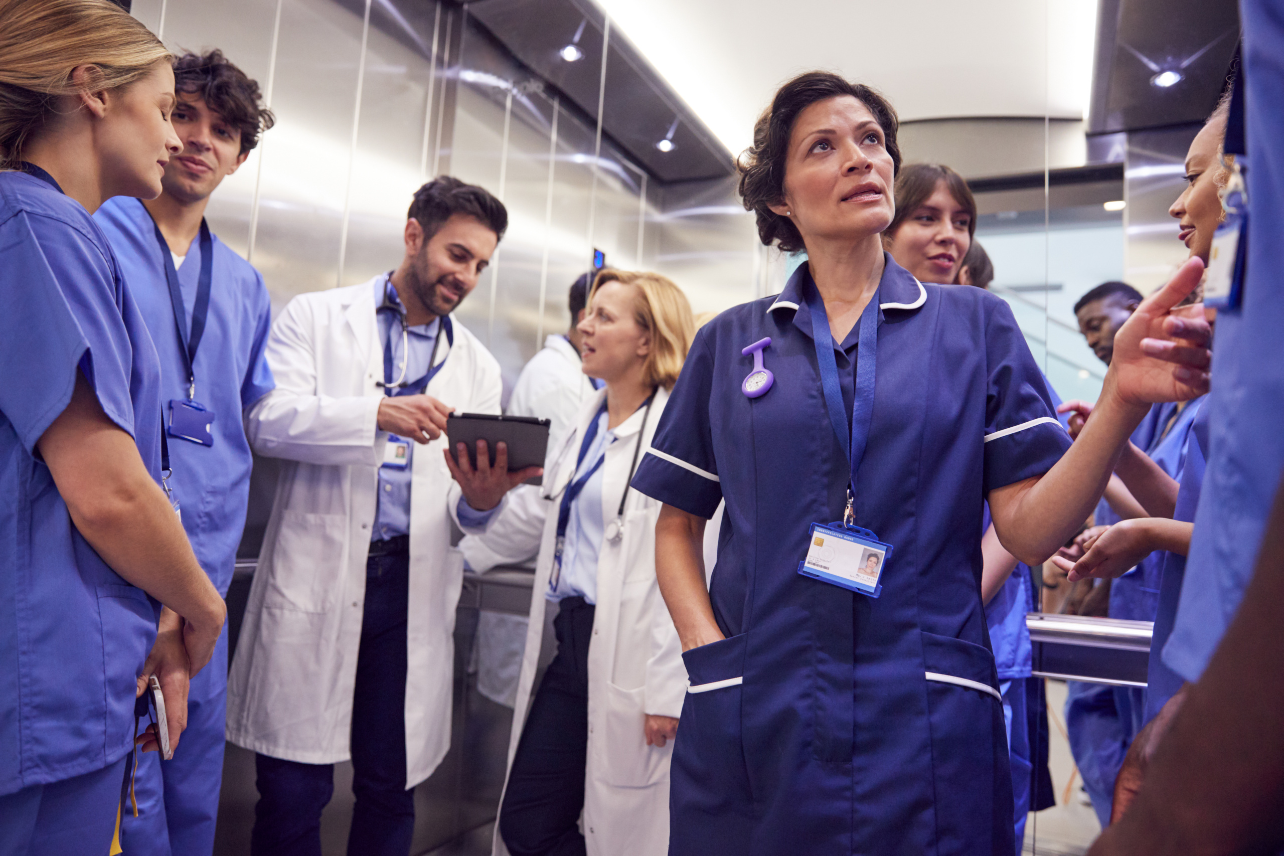 A group of temp healthcare staff hospital in elevator, two employees looking at tablet: The WorkTracker timesheet portal