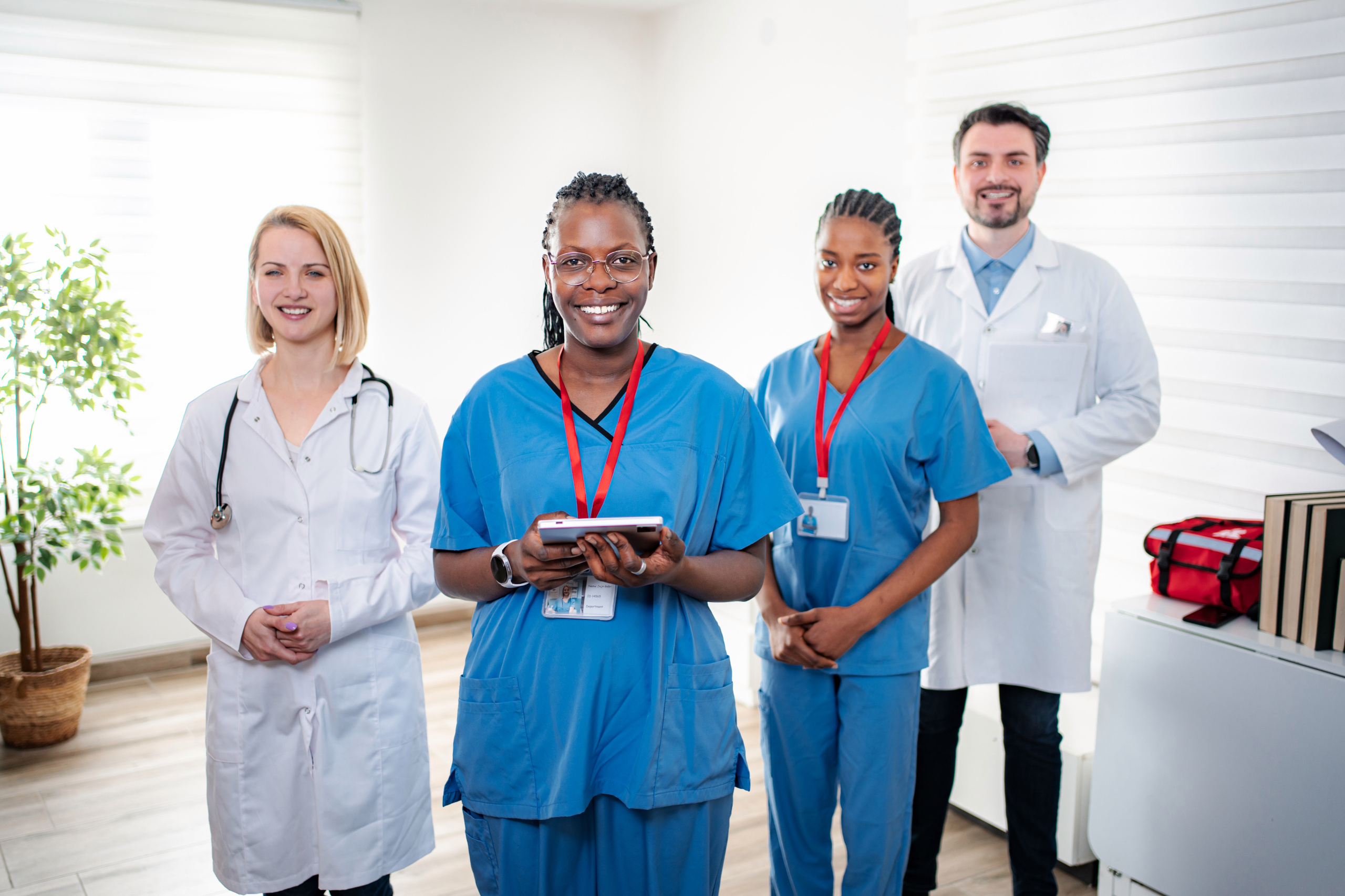 Four happy healthcare workforce, the foremost one holding a tablet: The YouRecruit workforce management system