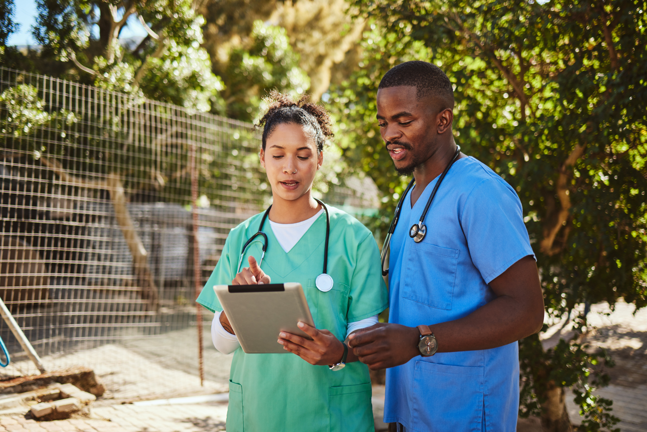Two temporary healthcare employees in outdoor location, one holding smart device discussing the WorkTracker job hours app