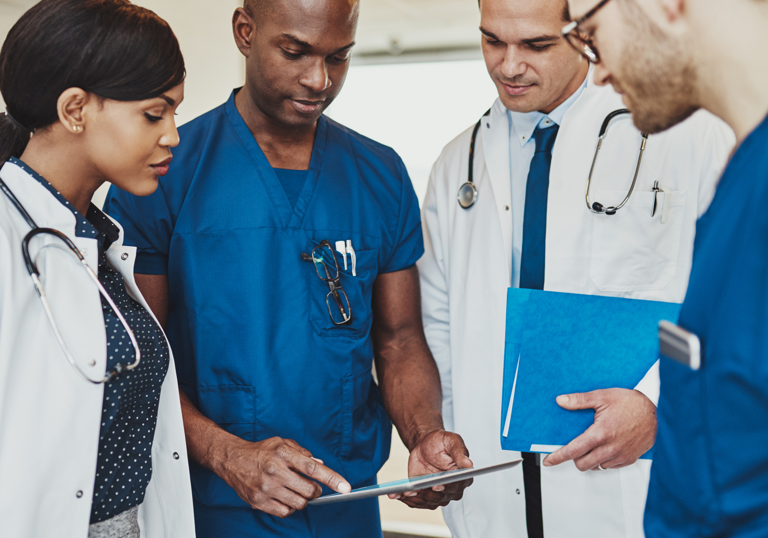 Team of healthcare workers discussing issues and grouped around a tablet: The YouRecruit recruitment agency software