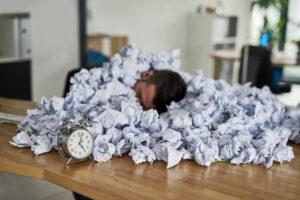 Man covered in crumpled up paper beside a clock representing paper timesheet errors: YouRecruit and WorkTracker timesheet app