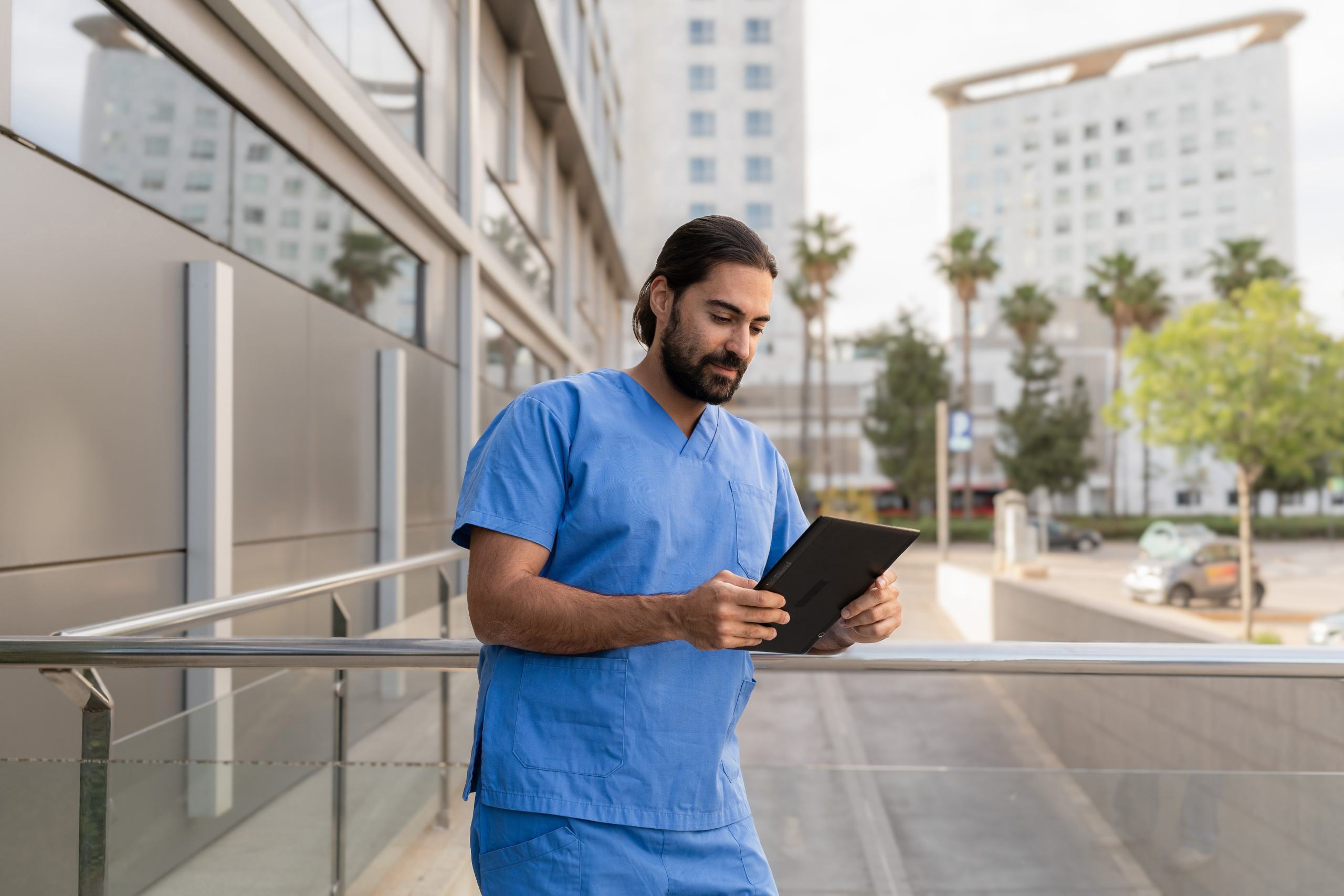 Male doctor in blue scrubs using digital tablet outside hospital: The WorkTracker mobile workforce management app