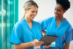 Two happy female doctors, one holding a tablet: The YouRecruit shift scheduling software and WorkTracker rota planner app